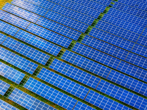 Aerial view of a modern solar park with rows of blue photovoltaic panels arranged in a grid pattern across a green field in Germany.