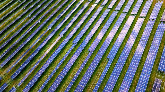 Aerial view of a modern solar park with rows of photovoltaic panels arranged in a geometric pattern over green grassy fields in Germany.
