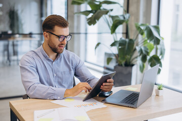 Obraz premium Professional man working on tablet and laptop in modern office, managing business data and focused on technology