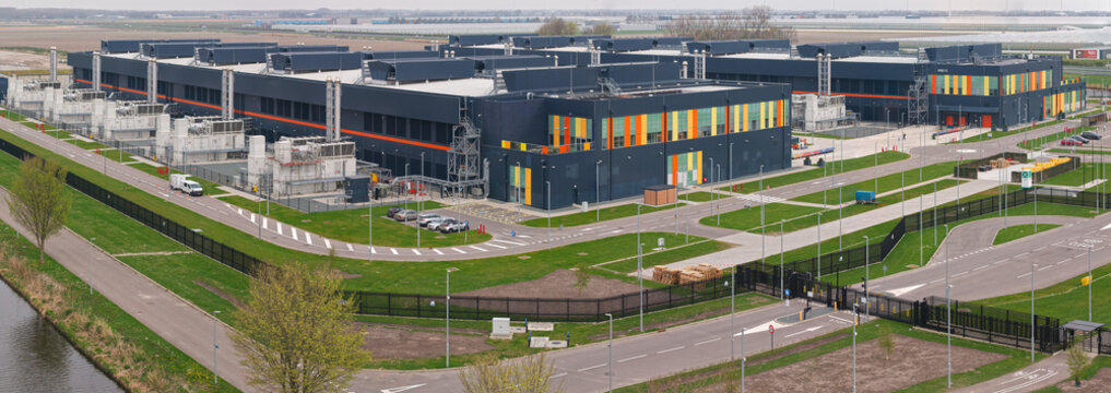 Aerial view of a large modern data center campus with industrial buildings, back-up energy infrastructure, and surrounding green fields in Middenmeer, Noord-Holland, Netherlands.