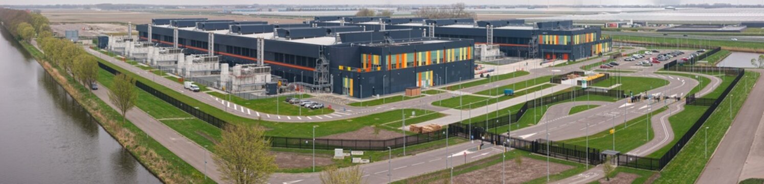 Aerial view of a large modern data center campus with industrial buildings, back-up energy systems, and parking areas situated in the polder landscape of Middenmeer, Noord-Holland, Netherlands.