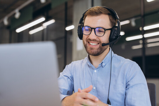 Male customer support agent wearing headset and glasses, smiling and providing online assistance on laptop