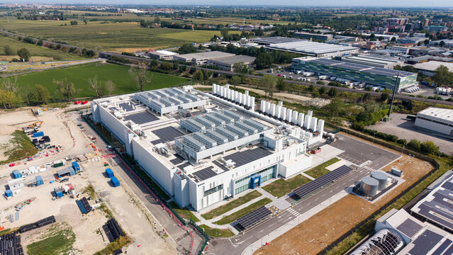 Aerial view of a modern data center campus with advanced digital infrastructure, rooftop solar panels, and surrounding industrial landscape in Melegnano, Lombardy, Italy.