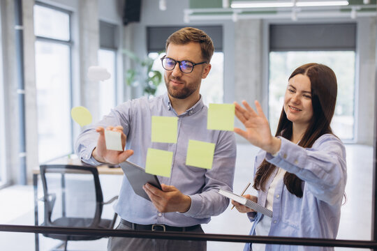 Business colleagues collaborating on an agile task board with sticky notes in a modern office, planning a project