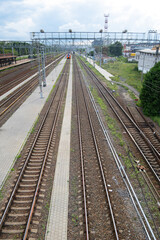 Obraz premium Tracks stretch into the distance at a railway station. Platforms stand empty under a cloudy sky. An electric train is moving in the distance.