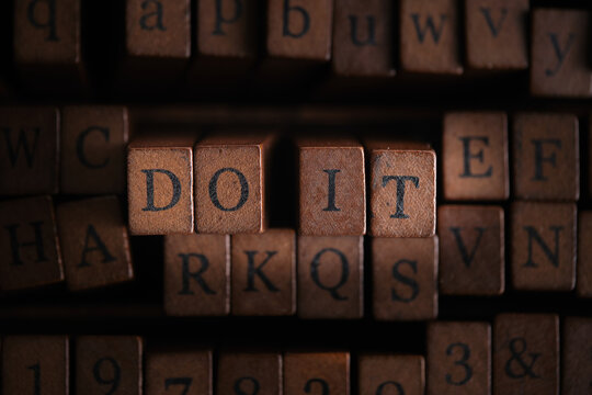 Motivational phrase DO IT composed retro wooden letter stamps surrounded by letterpress blocks.