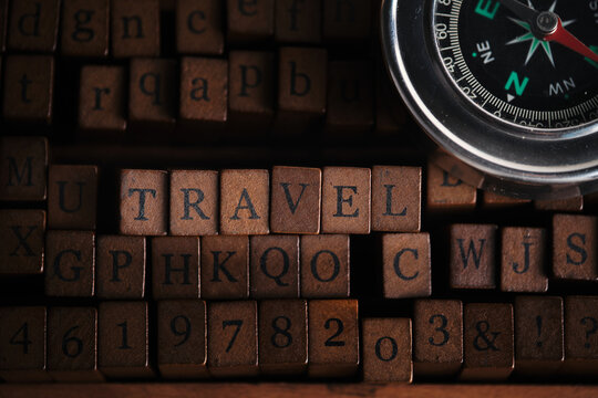 Word TRAVEL spelled with vintage wooden stamps alongside navigational compass on dark background.