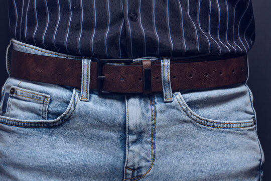 Close up shot man wearing light blue jeans with brown leather belt and striped shirt.