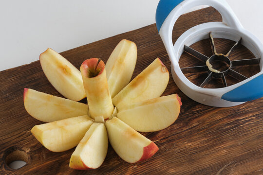 Sliced fresh red apple with core on wooden cutting board next to plastic manual slicer cutter.