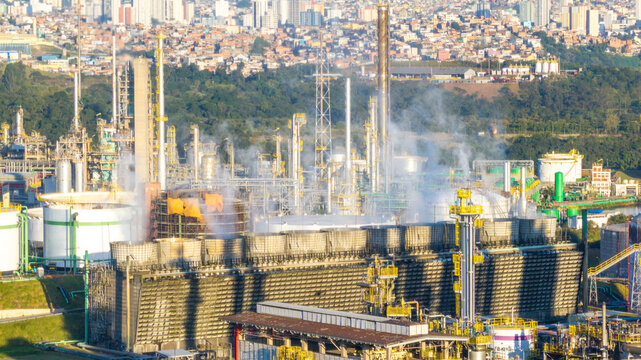 Aerial view of the petrochemical complex with industrial cooling towers, processing units, and smoke plumes set against an urban background in Santo Andre, State of Sao Paulo, Brazil.