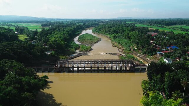 Aerial view of Jalaur Dam spanning the river with lush greenery and rural landscape in Dingle, Western Visayas, Philippines.