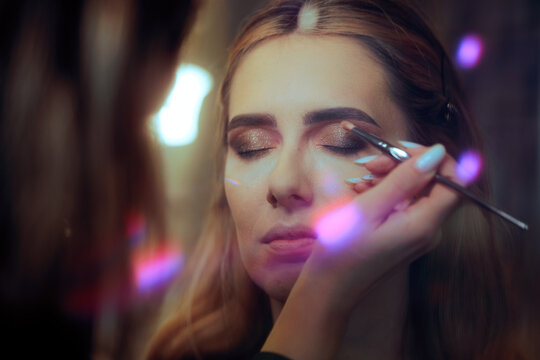 Glamour Makeup Application On Beautiful Female Model Close Up Shot. Professional artist applies shimmering eye shadow onto face of young woman during creative photo session