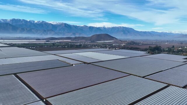 Aerial view of agricultural fields with rows of greenhouses under a blue sky near the Andes mountains in Santiago, Santiago Metropolitan, Chile.