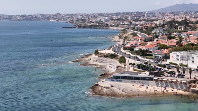 Aerial view of Praia das Avencas in Cascais, showing the coastline, sandy beach, coastal road, and urban buildings along the Atlantic Ocean in Cascais, Lisboa, Portugal.