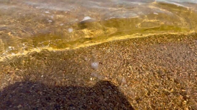 Crystal clear freshwater gently washing over the sandy shoreline on a sunny summer day. Close-up of transparent lake water with natural textures, ripples and peaceful outdoor atmosphere.
