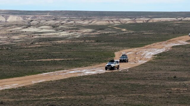 Aerial view of off-road vehicles driving on a dirt track through the vast, arid landscape of the Bozjyra desert in Aktau, Mangystau Region, Kazakhstan.