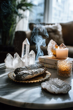 Smoldering white sage with quartz crystal healing stones and lit candle in a calm wellness home interior