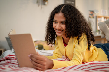 African American teenage girl lying on comfort bed and reading a book.  © Kawee