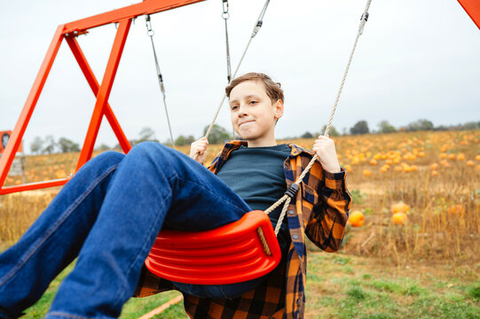 Teen boy relaxing on a swing beside a pumpkin patch in autumn