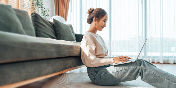 Young Asian woman working from home. Freelancer businesswoman using laptop at sunny room. Student female learning and working at home