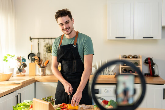 Latino man live streaming with mobile phone while cooking food in kitchen.