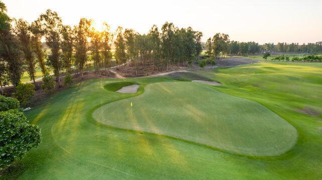 Flying drone view over a spacious empty golf course with green grass and rolling hills. 