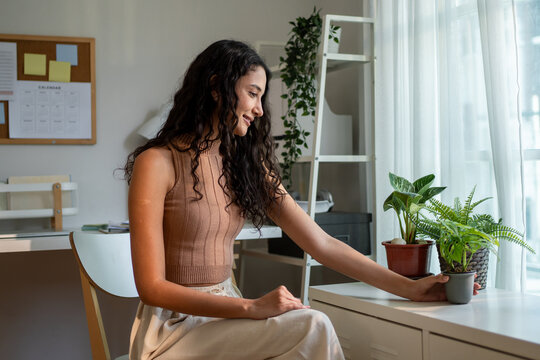 Young Hispanic woman gently taking care of indoor plants in cozy house. 