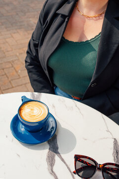 young woman with a cup of coffee, latte at outdoor cafe with sunglasses on the table