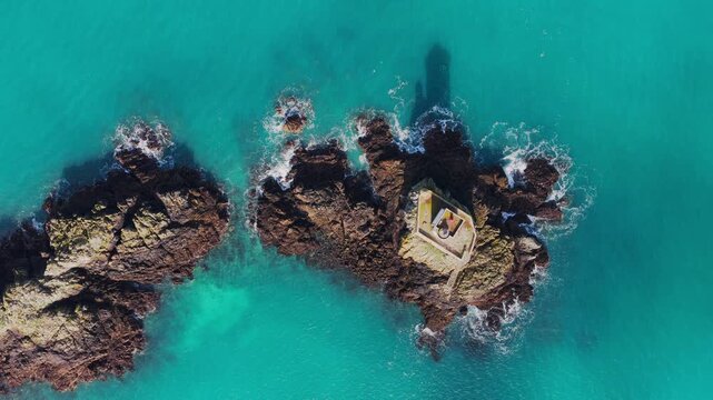 Aerial view of Phare de L'Ost-Pic lighthouse on a rocky outcrop surrounded by turquoise sea water in Plouezec, France.