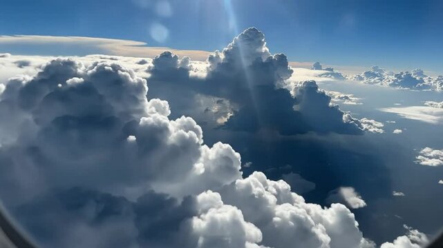 Epic High Altitude View of Cumulus Clouds from Airplane Window with Bright Blue Sky and Sun Glare