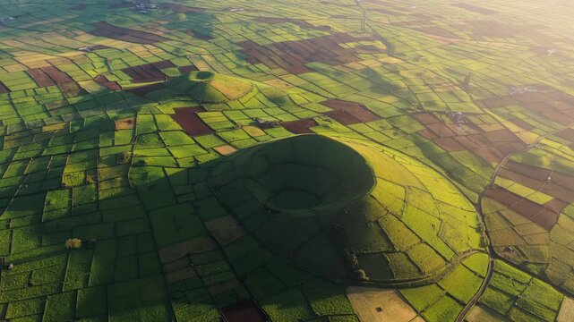 Aerial view of volcanic craters surrounded by lush green patchwork fields and stone walls in Terceira, Azores, Portugal.
