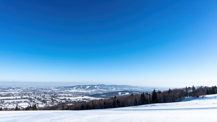 Obraz premium Winter Landscape: A panoramic view of a snow-covered landscape with a distant town nestled amongst rolling hills and a clear blue sky above.
