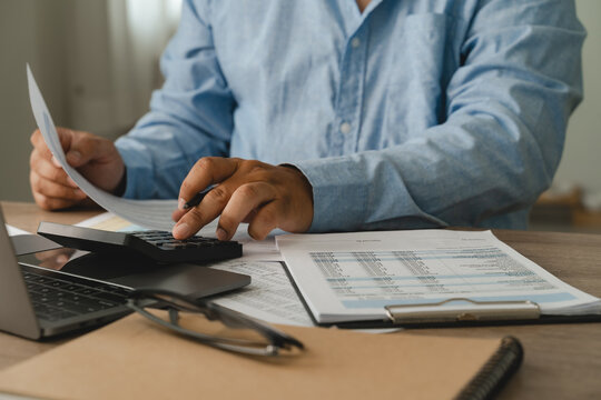 Reviewing financial paperwork and pressing a calculator beside a laptop and clipboard for accounting analysis and report preparation, hands check printed figures and tables on a desk.