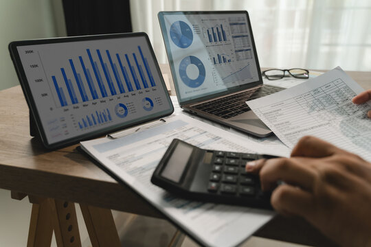 business data analysis to plan reports with a calculator while tablet and laptop display charts, showing business data analysis planning workflow for financial reporting document review.
