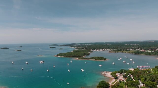 Aerial view of the Vrsar coastline featuring numerous boats anchored in the turquoise bay surrounded by lush green islands and forests in Vrsar, Istria County, Croatia.