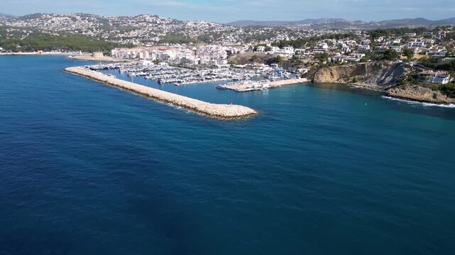 Aerial view of the marina in Moraira with numerous yachts and boats docked along the breakwater, surrounded by coastal buildings and the Mediterranean Sea in Moraira, Valencian Community, Spain.