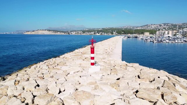 Aerial view of the stone breakwater with a red and white beacon at the marina in Moraira, Valencian Community, Spain.