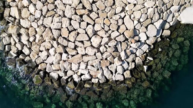 Aerial view of the rocky breakwater and clear sea water along the coast in Moraira, Valencian Community, Spain.