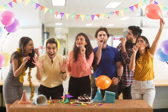 Group of colleagues blowing party hooters during new year celebration in office.