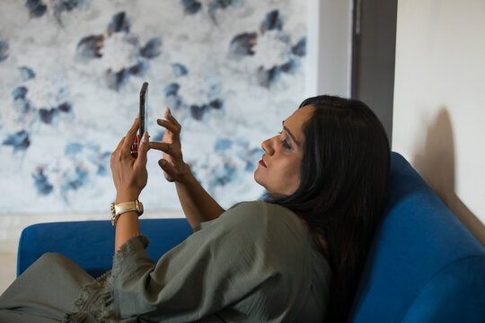 Woman sitting on the couch and checking her phone at home. 