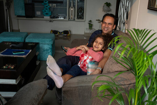 Young girl resting with her father on the sofa at home. 