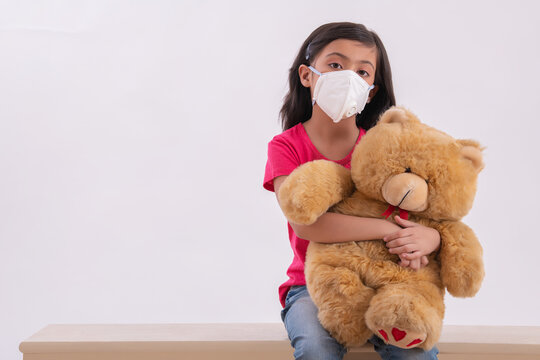 Young girl playing with her teddy bear inside wearing a pollution mask. (Children) 