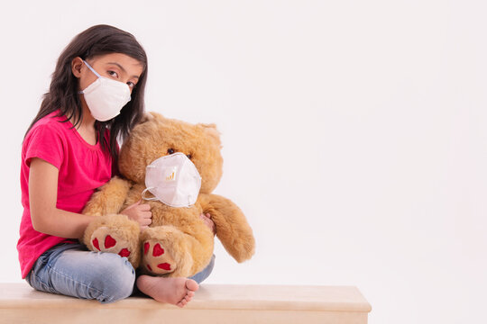 Young girl wearing a pollution mask and putting another on her teddy bear. (Children) 