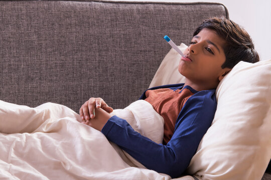 Young boy lying on sofa with thermometer in his mouth. (Children)