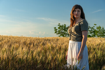 Obraz premium Young woman standing in golden wheat field at sunset