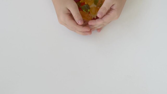 Child draws colorful gummy bears toward hands on clean white background. Sweet snack temptation, mindful nutrition, sugar intake in childhood and balanced eating concept.