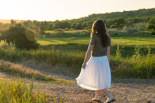 Young woman in white skirt walking on country road at sunset
