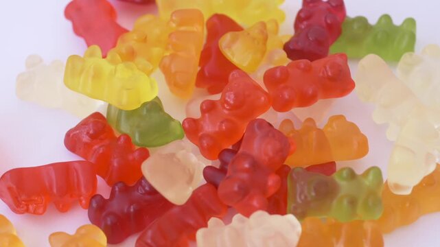 Bright jelly candies slowly rotate across white background creating vibrant food texture. Sweet craving, food temptation, dessert variety and colorful confectionery concept.