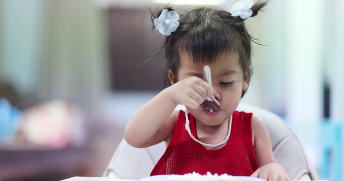 Asian toddler eating with a spoon independently, self-feeding, child development, healthy nutrition, baby weaning, early learning, growth, and independent eating skills