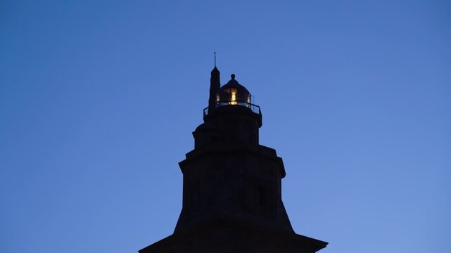 Detalle de la parte alta del faro de la Torre de H&eacute;rcules de noche, iluminado y en funcionamiento sobre el paisaje costero de A Coru&ntilde;a.